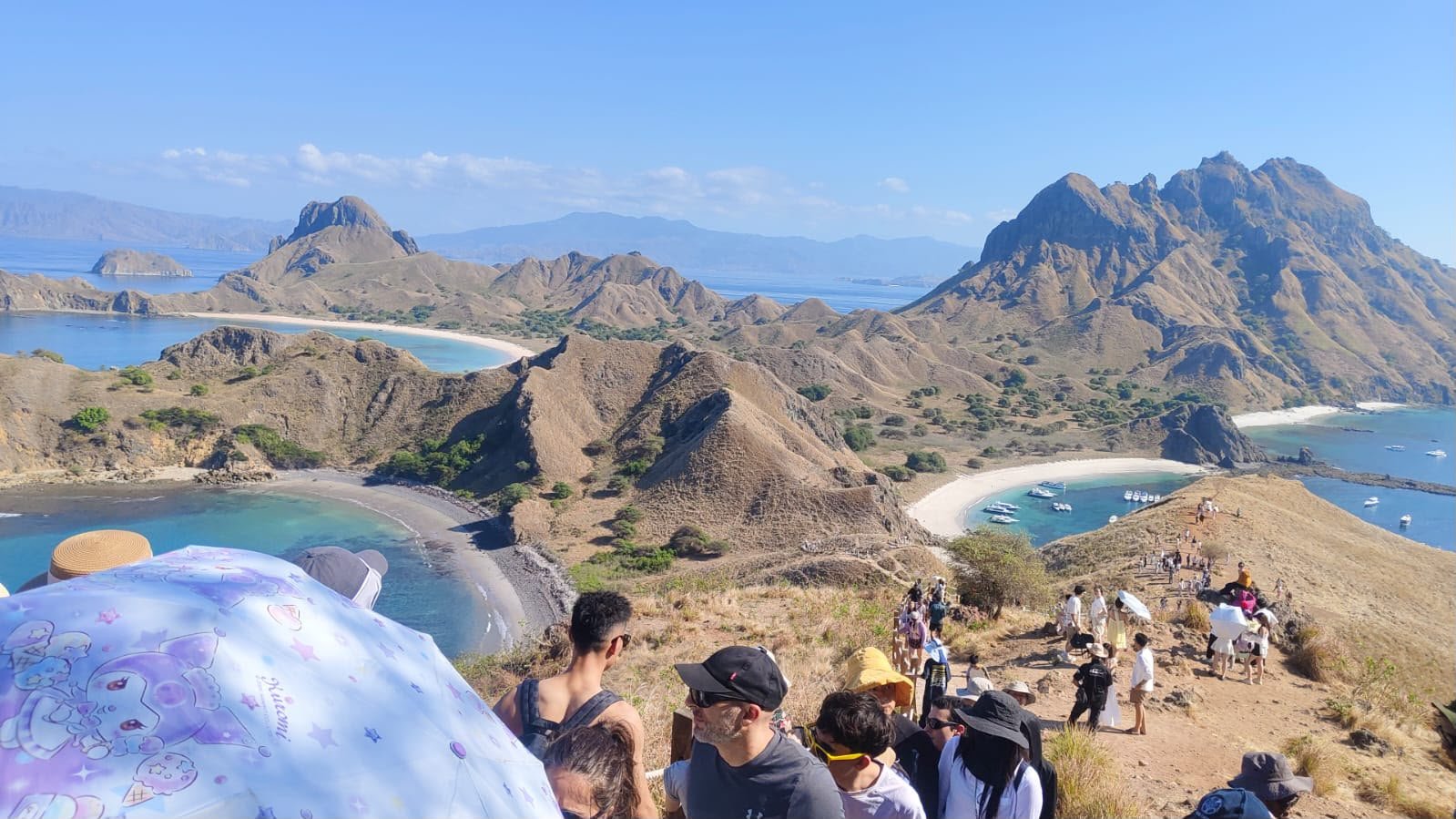 Panoramic view from the Padar Island ridge over bays and anchored boats, with visitors on the trail