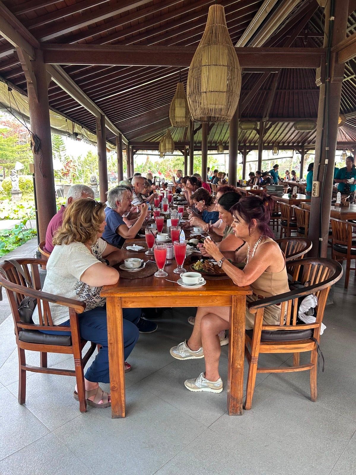 Members of the Portuguese group having lunch together at long wooden tables in the open pavilion of Bebek Joni Restaurant, Peliatan